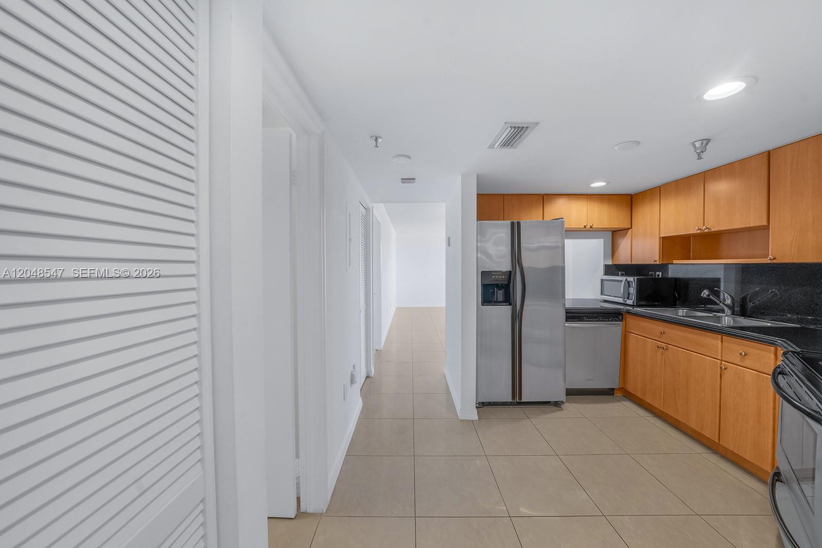 A kitchen with wooden cabinets, stainless steel appliances, and tile flooring leads to a hallway — 2400 SW 3rd Ave # 706, Miami FL 33129, MIAMI, FL