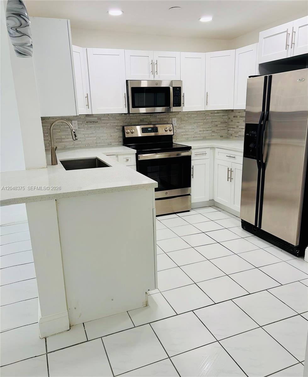 A kitchen features white cabinets, stainless steel appliances, quartz countertops, and white tile flooring — 5705 W 20th Ave # 101, Hialeah FL 33012, HIALEAH, FL