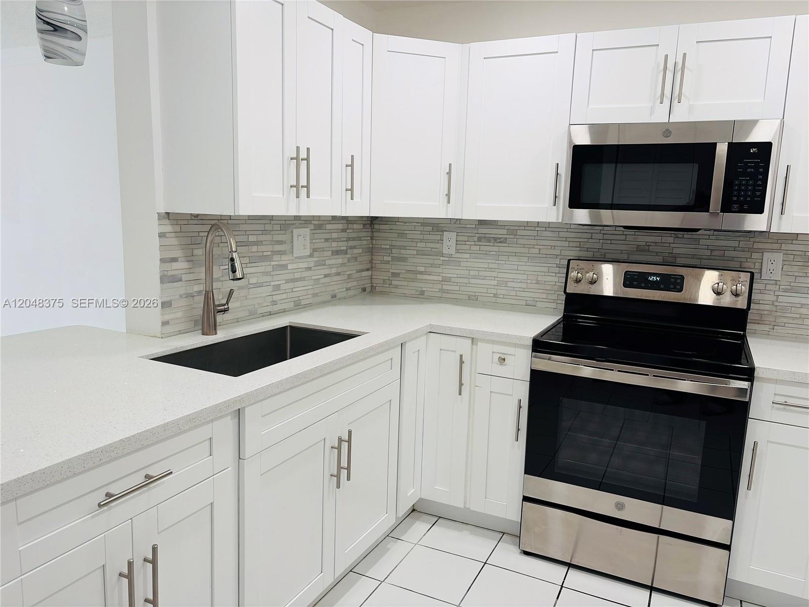 A kitchen features white shaker cabinets, stainless steel appliances, and a light-colored quartz countertop — 5705 W 20th Ave # 101, Hialeah FL 33012, HIALEAH, FL