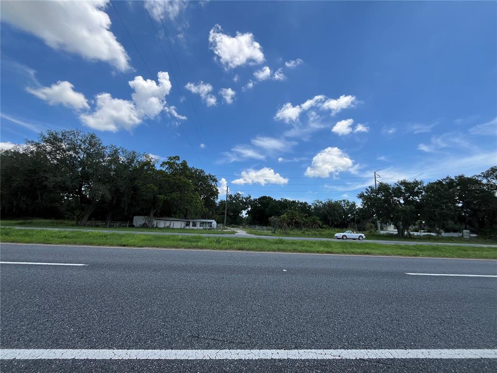 A view of a grassy lot with trees and a small structure from a road — 411 ALIBRANDI ROAD, LEESBURG, FL