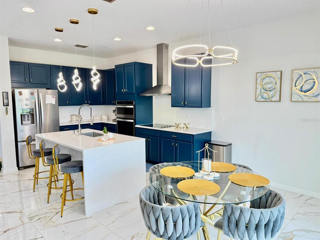 A kitchen features navy blue cabinets, a white quartz island, and a glass dining table — 1732 FLOURISH AVENUE, KISSIMMEE, FL