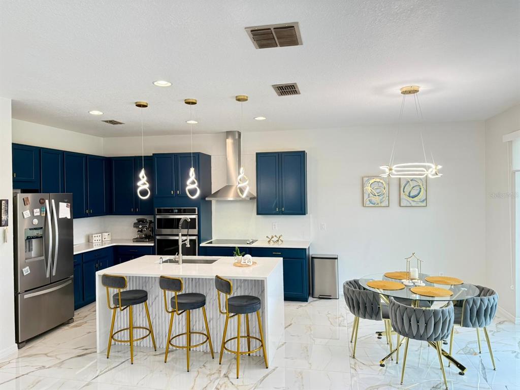 A modern kitchen features blue cabinets, a white marble island, and an adjacent dining area — 1732 FLOURISH AVENUE, KISSIMMEE, FL