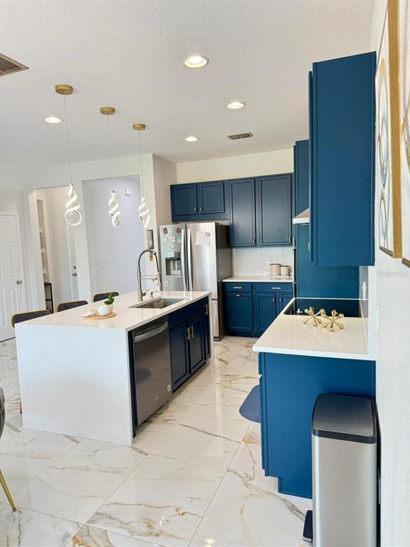 A kitchen features blue cabinets, white countertops, a central island, and white marble-look tile flooring — 1732 FLOURISH AVENUE, KISSIMMEE, FL