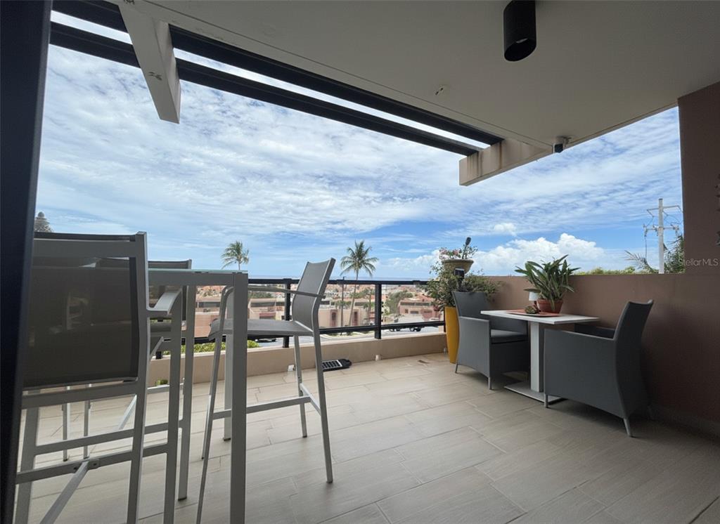 A covered balcony features tile flooring, outdoor furniture, and a view of the distant ocean — 170 PALMAS  DRIVE DRIVE UNIT B14, HUMACAO, PR