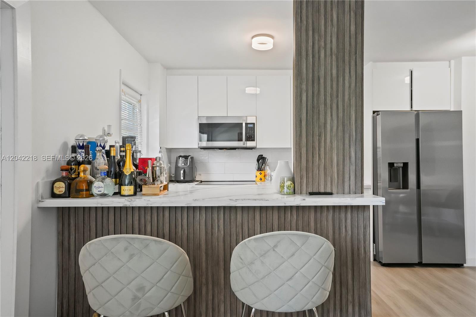 A kitchen features white cabinets, a marble-look countertop, and a wood-slatted breakfast bar — 1614 West Ave # 203, Miami Beach FL 33139, MIAMI BEACH, FL