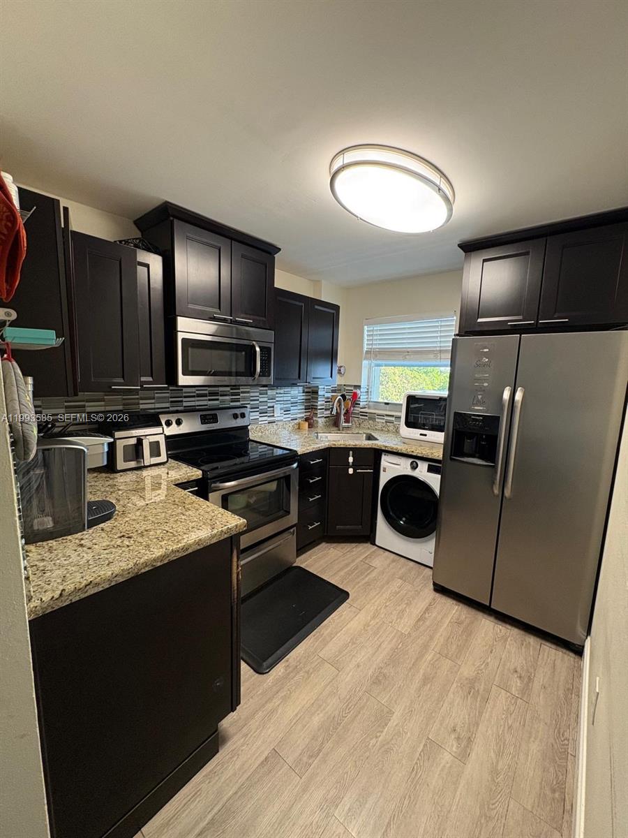A kitchen features dark wood cabinets, granite countertops, stainless steel appliances, and a front-loading washer — 910 Michigan Ave # 505, Miami Beach FL 33139, MIAMI BEACH, FL