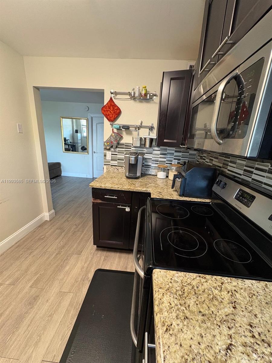 A kitchen features dark wood cabinets, granite countertops, stainless steel appliances, and a tiled backsplash — 910 Michigan Ave # 505, Miami Beach FL 33139, MIAMI BEACH, FL