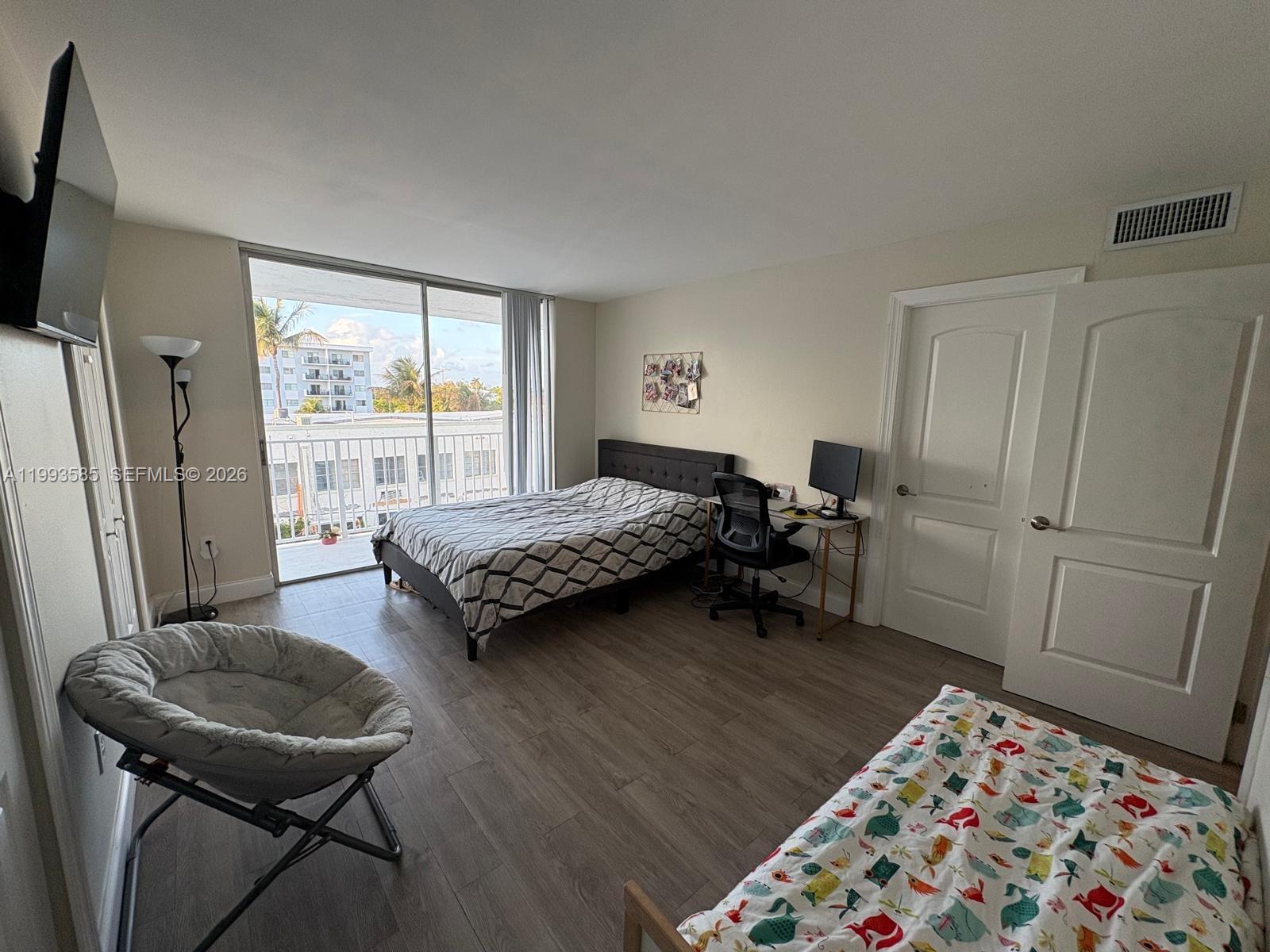 A bedroom features two beds, a desk, a balcony, and light wood-look flooring — 910 Michigan Ave # 505, Miami Beach FL 33139, MIAMI BEACH, FL