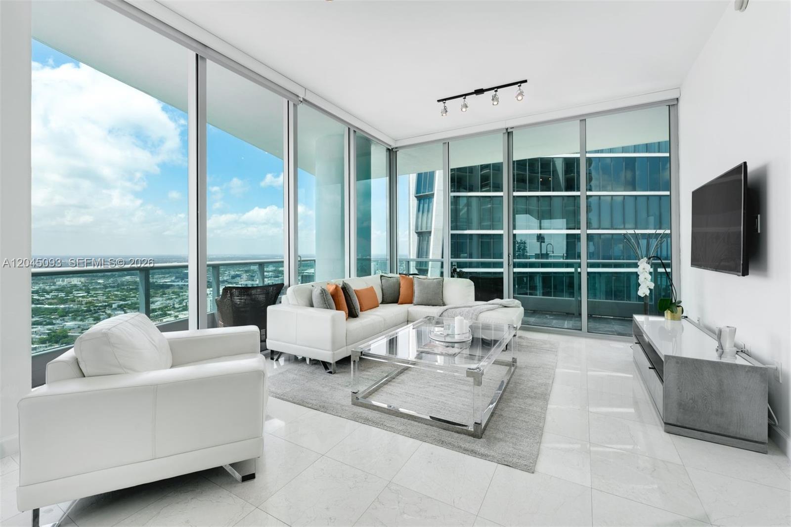 A modern living room features white furniture, a glass coffee table, and floor-to-ceiling windows — 900 Biscayne Blvd # 5812, Miami FL 33132, MIAMI, FL