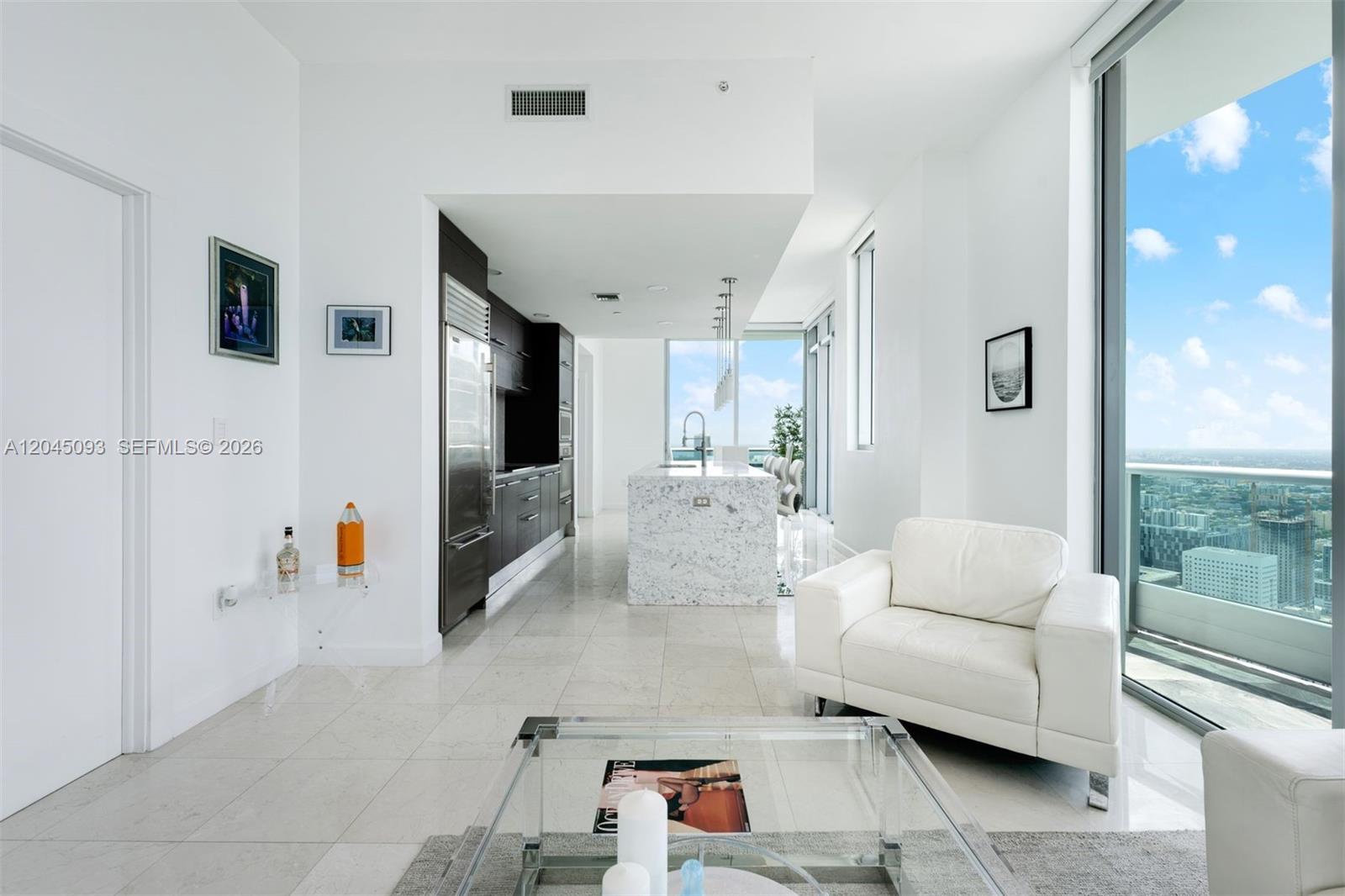 A modern kitchen with a marble island and white cabinetry overlooks a high-rise city view — 900 Biscayne Blvd # 5812, Miami FL 33132, MIAMI, FL