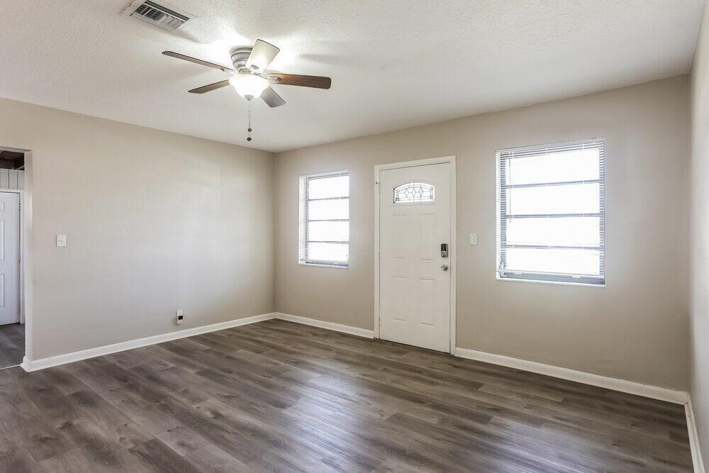 An empty room features light-colored walls, wood-look flooring, a ceiling fan, and a front door — MIAMI GARDENS, FL