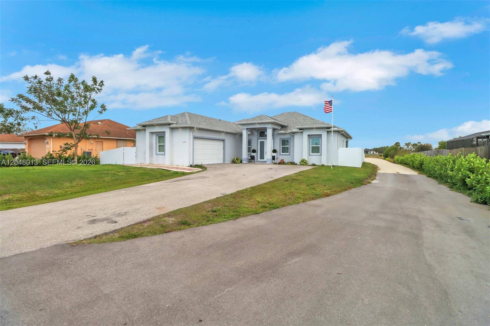 A light-colored single-story house with a garage, a paved driveway, and an American flag — 2394 45th Avenue NE, Naples FL 34120, NAPLES, FL