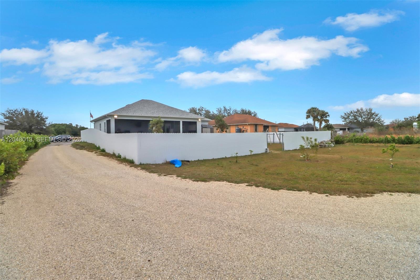 A gravel driveway leads to a house enclosed by a white vinyl privacy fence — 2394 45th Avenue NE, Naples FL 34120, NAPLES, FL