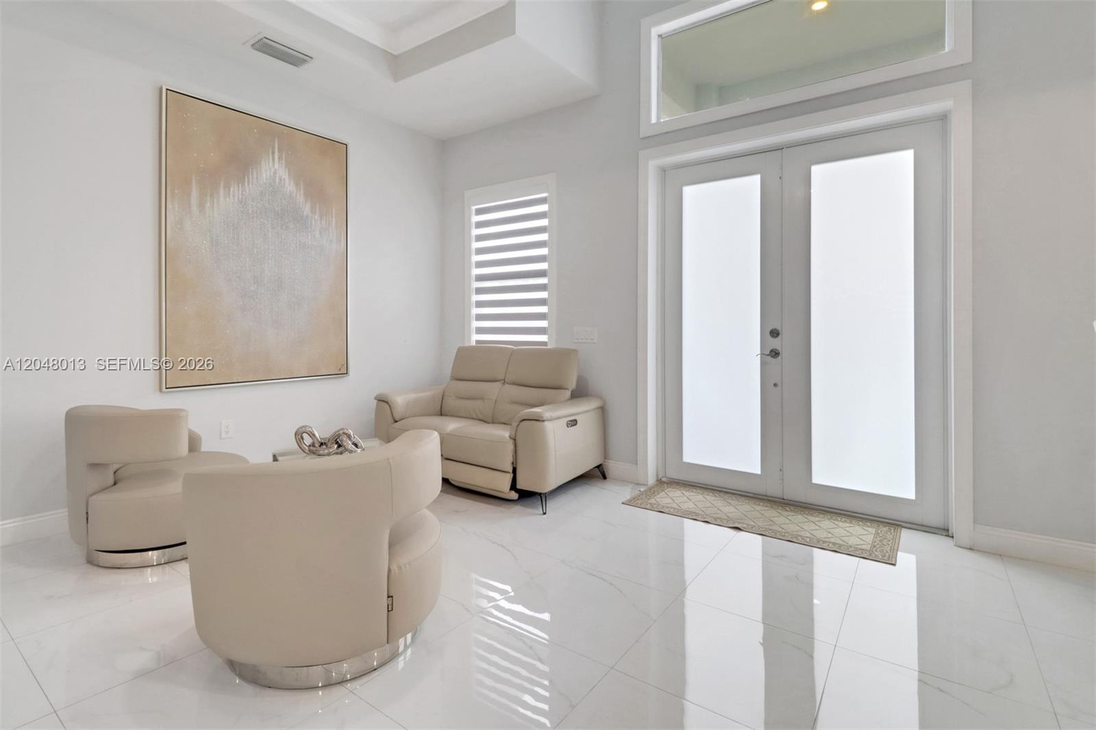 A modern living room features white tile floors, beige seating, and a large abstract painting — 2394 45th Avenue NE, Naples FL 34120, NAPLES, FL
