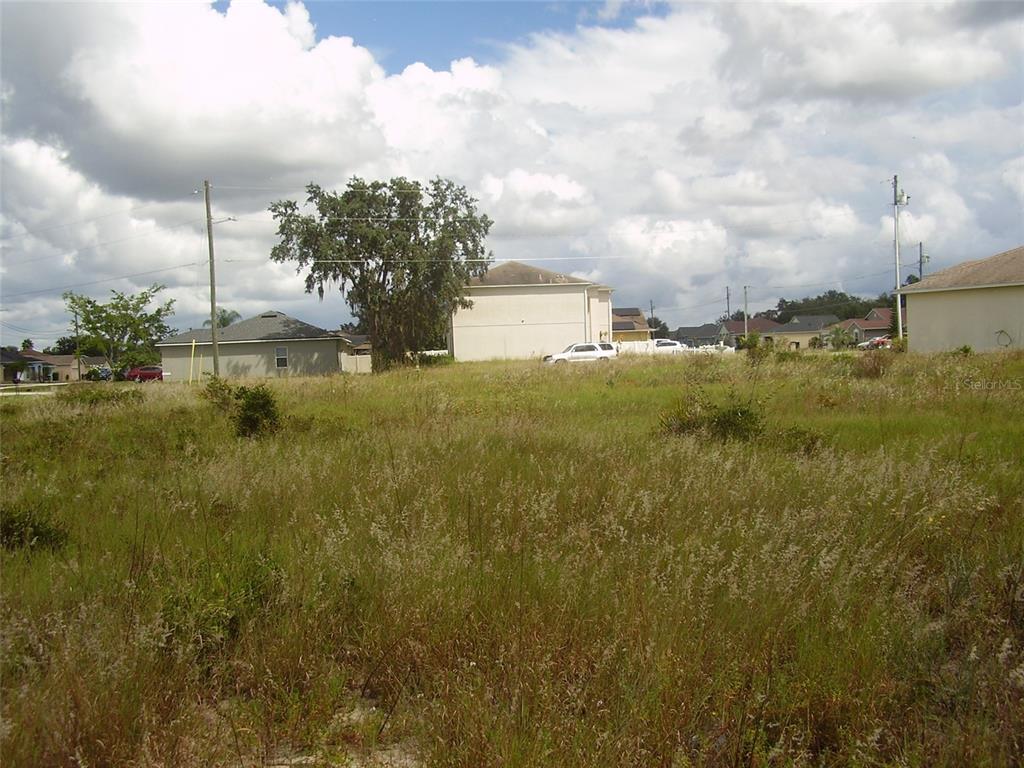 A vacant, grassy residential lot sits in front of several suburban houses under a cloudy sky — 1943 MANATEE DRIVE, KISSIMMEE, FL