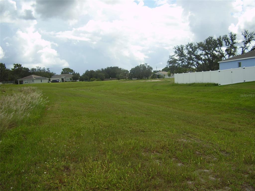 A grassy, sloped vacant lot is bordered by a white fence and neighboring houses — 1943 MANATEE DRIVE, KISSIMMEE, FL