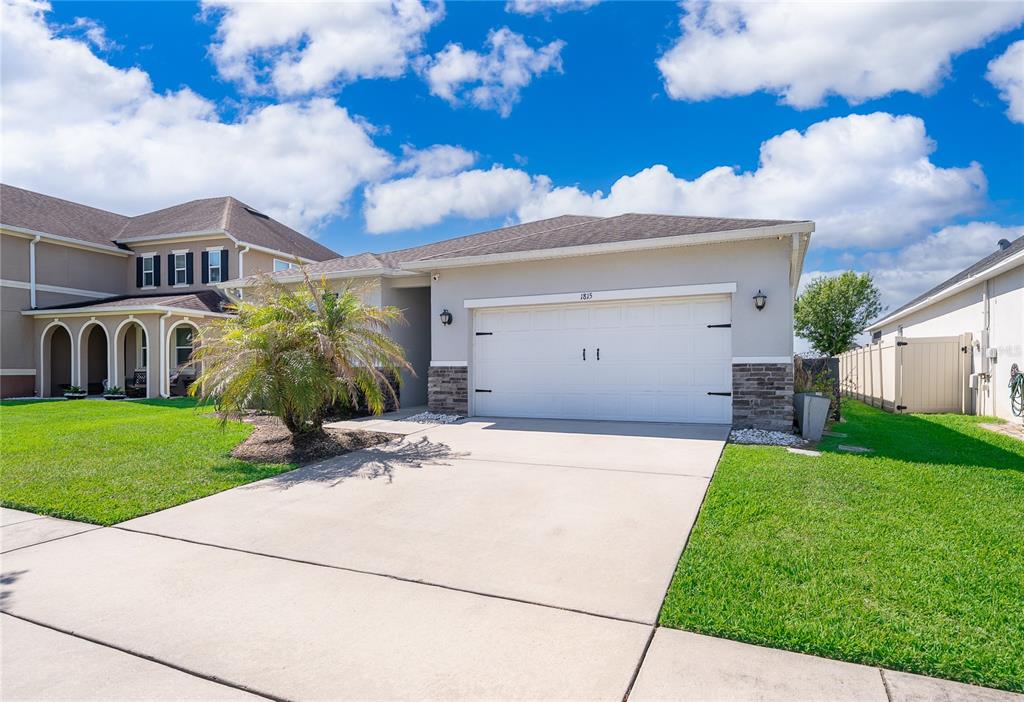 A single-story house with a two-car garage, stone accents, and a palm tree in front — 1815 PLUMAS WAY, ORLANDO, FL