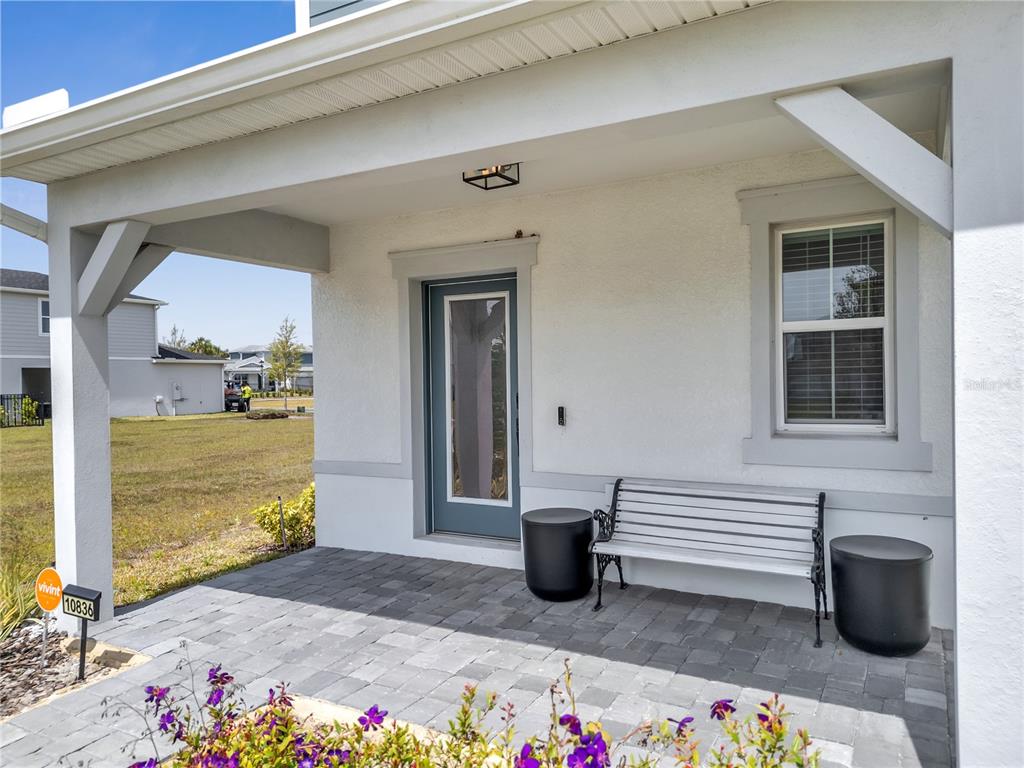 A covered front porch features gray pavers, a white bench, and a blue front door — 10836 WATERWOOD ALLEY, ORLANDO, FL