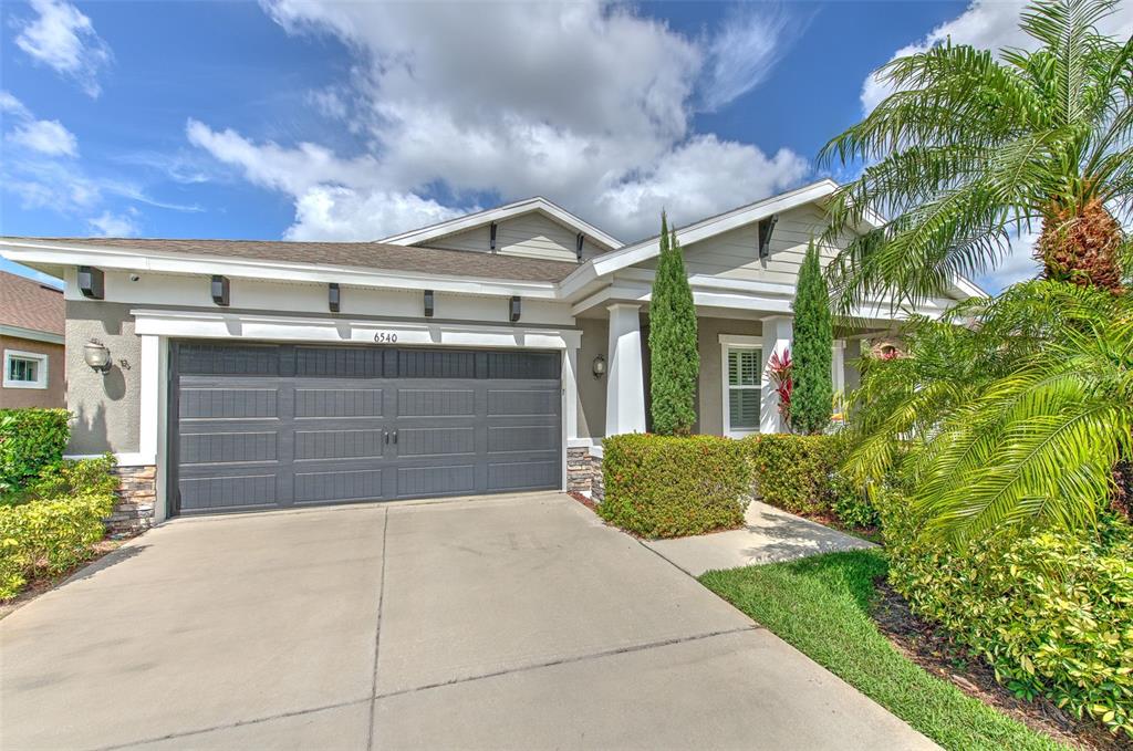 A suburban house exterior features a gray garage, a concrete driveway, and landscaped front yard — 6540 PARK STRAND DRIVE, APOLLO BEACH, FL