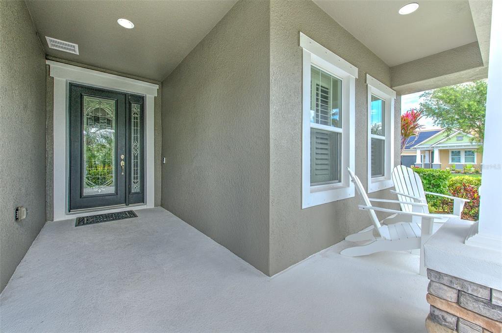 A covered front porch features a dark glass-paneled door, two white chairs, and gray walls — 6540 PARK STRAND DRIVE, APOLLO BEACH, FL