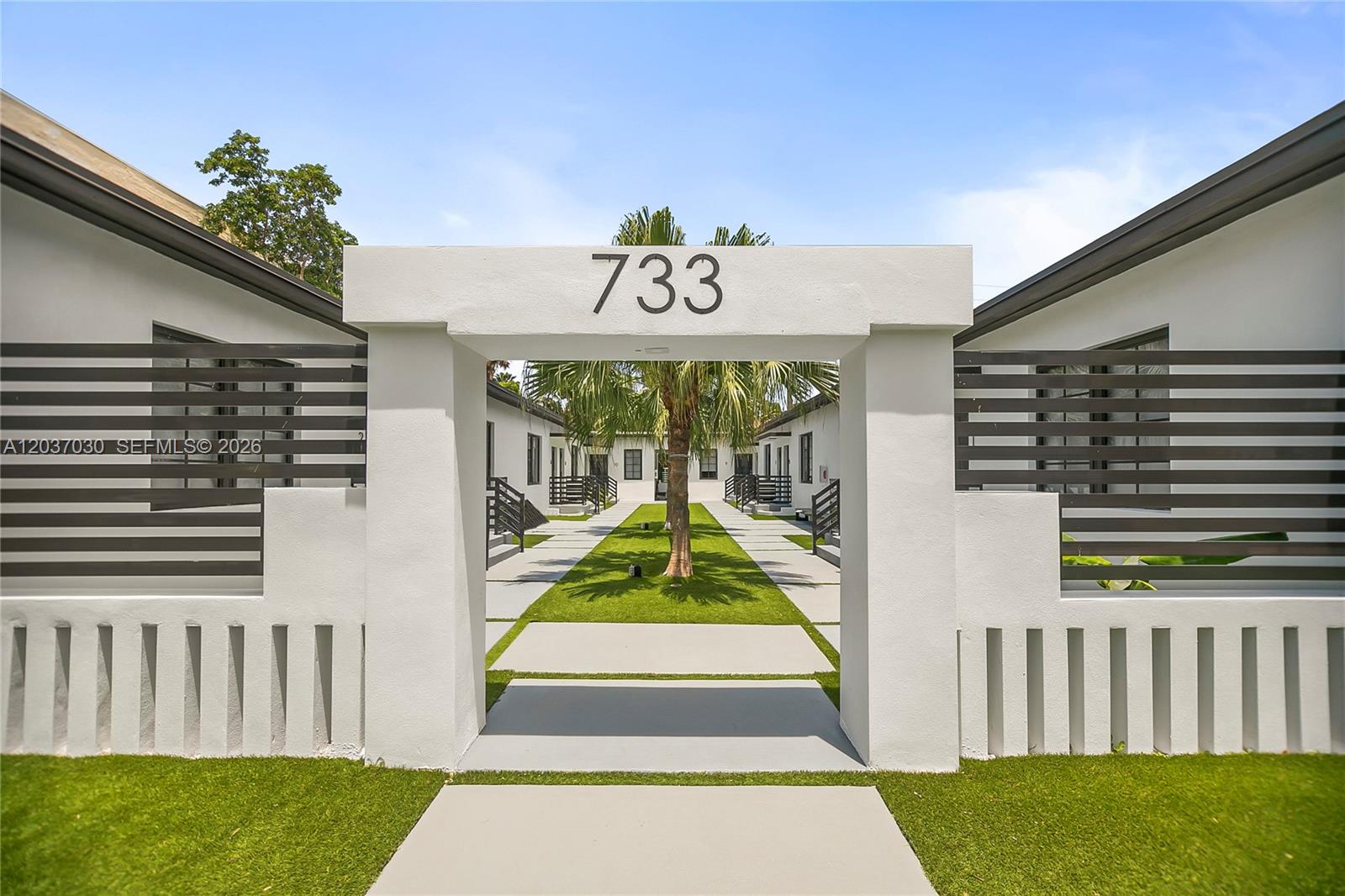 A white stucco entryway with the number 733 leads to a landscaped courtyard between buildings — MIAMI BEACH, FL
