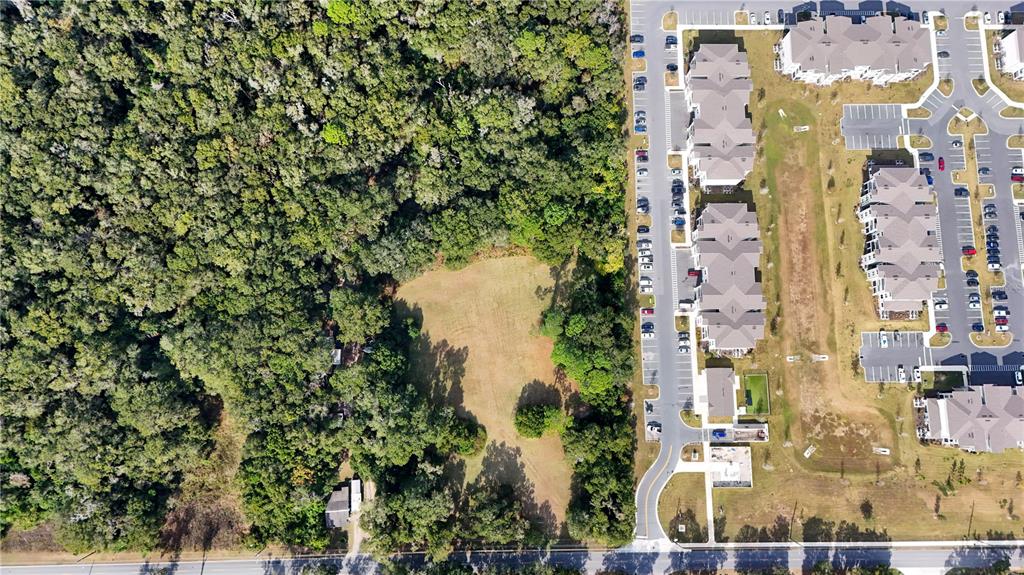 An aerial view shows a cleared grassy lot adjacent to a dense forest and apartments — 2495 NW NW 21ST STREET, OCALA, FL