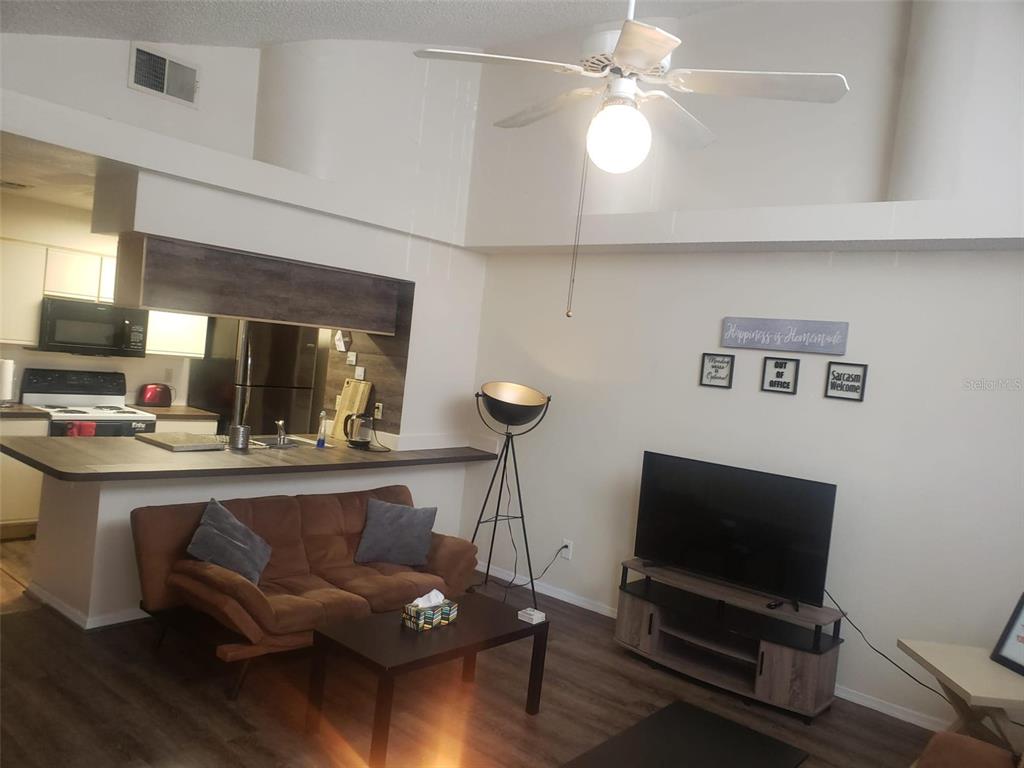 A living room with a brown sofa, television, and an open kitchen with a breakfast bar — 2478 SWEETWATER CLUB CIRCLE UNIT 94, KISSIMMEE, FL