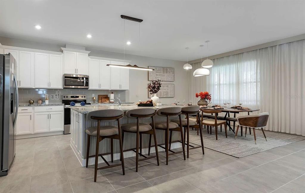 A modern kitchen and dining area features white cabinetry, a large island, and tile flooring — 2312 SALTY WINDS WAY, KISSIMMEE, FL