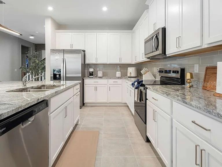 A modern kitchen features white cabinetry, stainless steel appliances, and granite countertops — 2312 SALTY WINDS WAY, KISSIMMEE, FL
