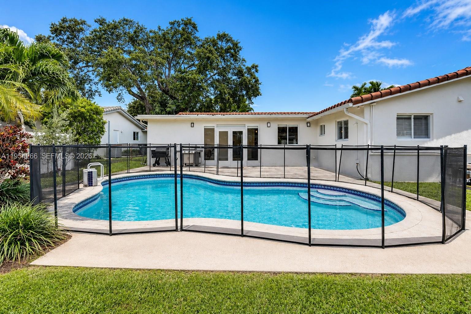 A backyard features a swimming pool enclosed by a black safety fence near a house — 3671 N 47th Ave, Hollywood FL 33021, HOLLYWOOD, FL