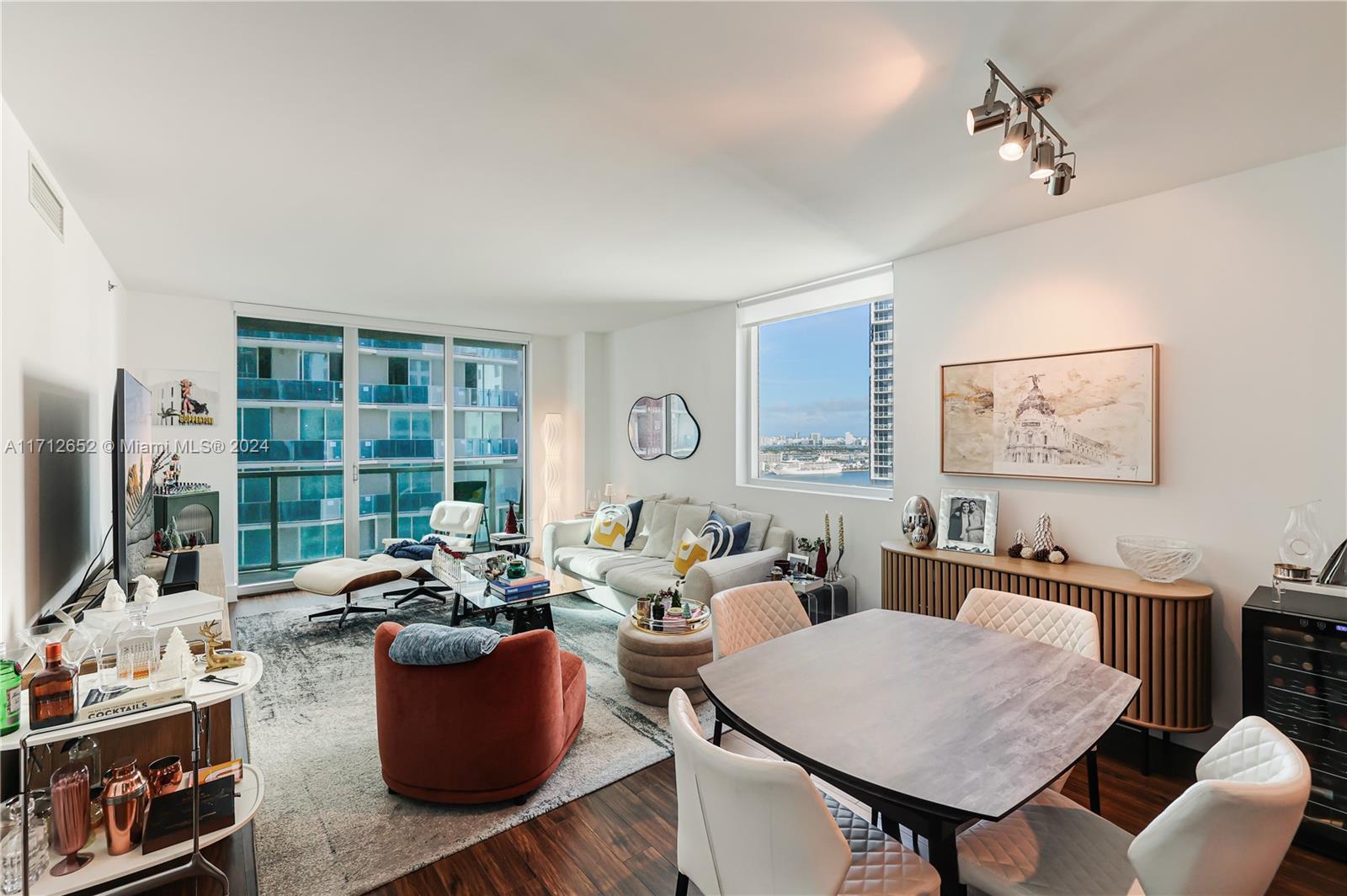 A modern living and dining area features hardwood floors, floor-to-ceiling windows, and a city view — 55 SE 6th St # 3407, Miami FL 33131, MIAMI, FL