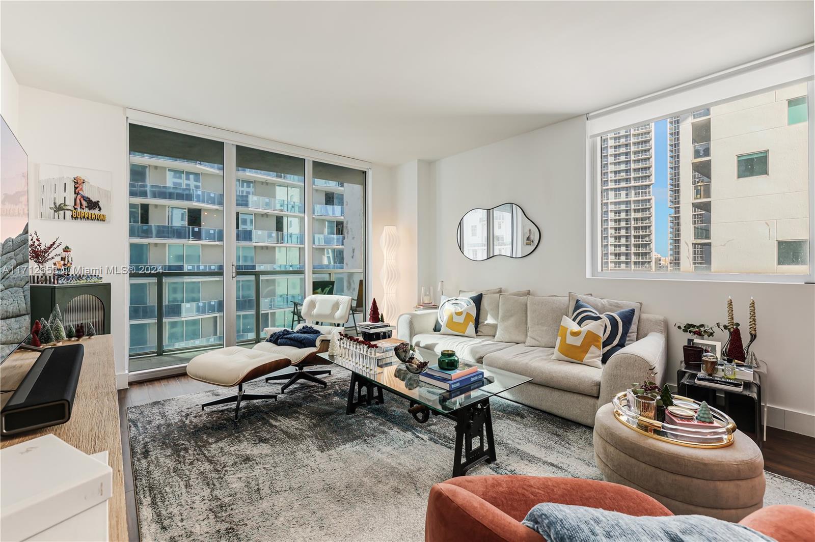 A modern living room features a glass coffee table, cream sofa, lounge chair, and large windows — 55 SE 6th St # 3407, Miami FL 33131, MIAMI, FL