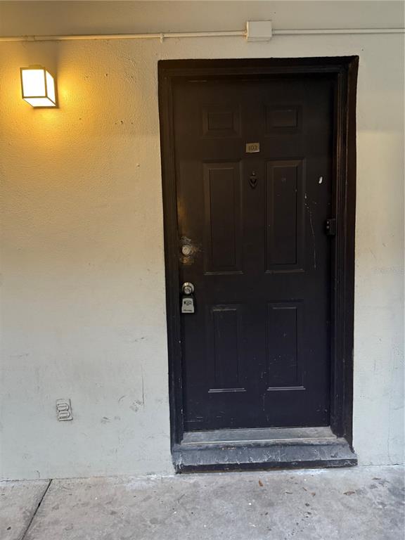 A dark-colored apartment door with a lockbox and a wall-mounted light fixture — 1264 113TH AVENUE UNIT J102, TAMPA, FL