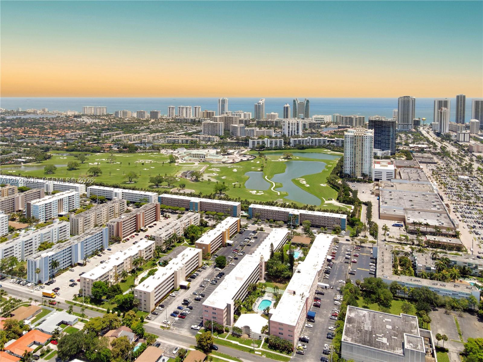 An aerial view shows residential apartment buildings, a golf course, and a distant city skyline — 180 NE 12th Ave # 18C, Hallandale Beach FL 33009, HALLANDALE BEACH, FL