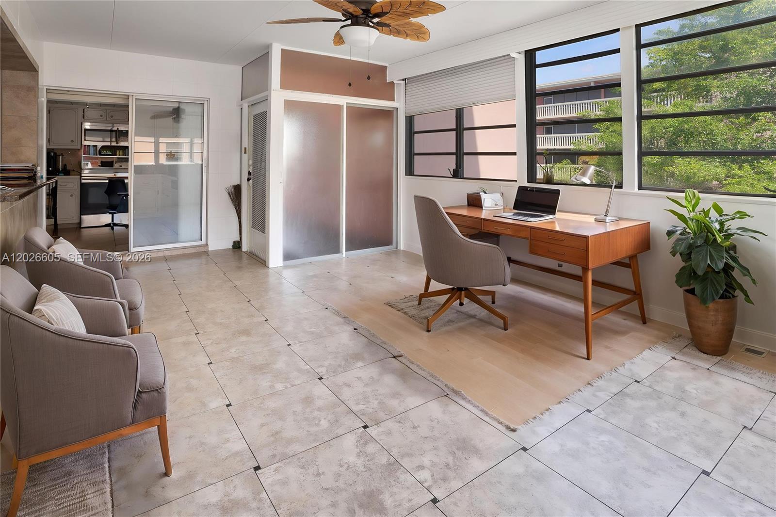 A sunroom features tile flooring, a wooden desk, two armchairs, and large windows — 180 NE 12th Ave # 18C, Hallandale Beach FL 33009, HALLANDALE BEACH, FL