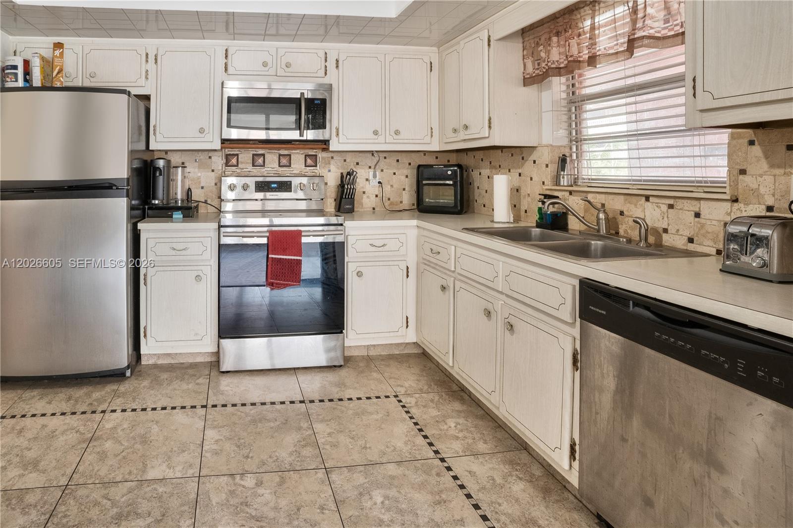 A kitchen features white cabinets, stainless steel appliances, a tiled backsplash, and light-colored floor tiles — 180 NE 12th Ave # 18C, Hallandale Beach FL 33009, HALLANDALE BEACH, FL
