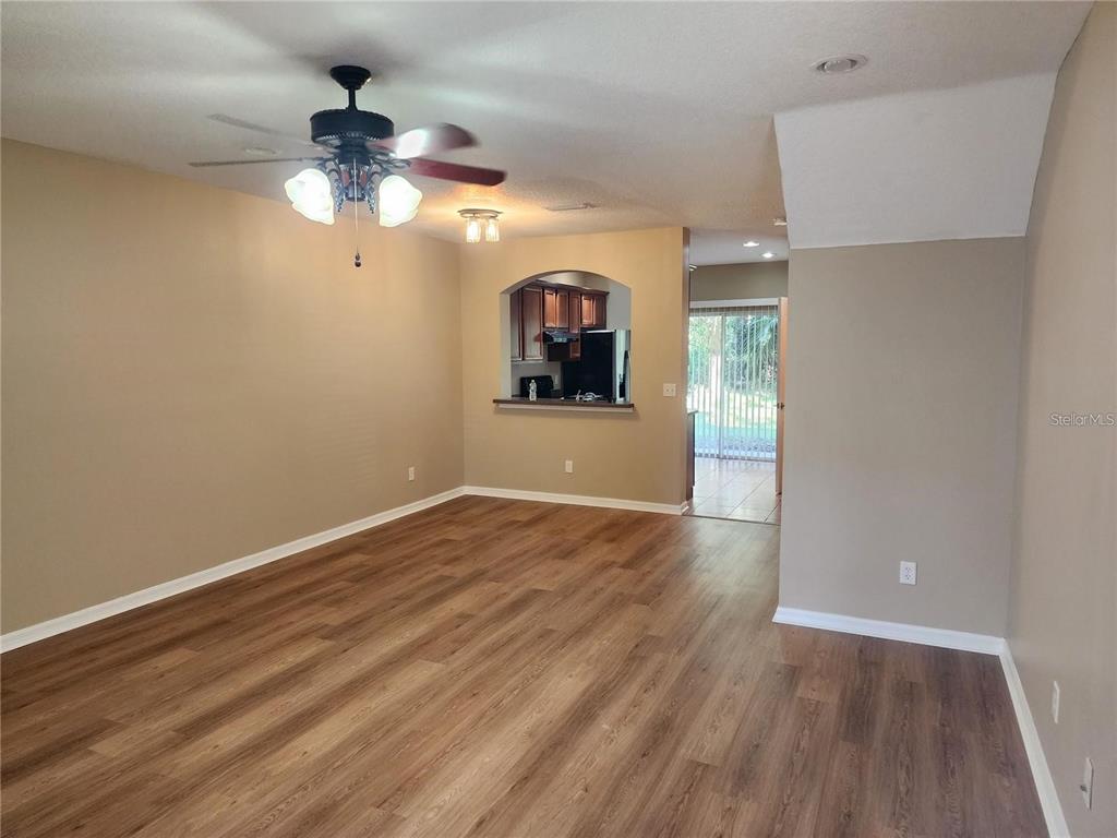 An empty living room features wood-look flooring, tan walls, a ceiling fan, and a pass-through — 15924 FISHHAWK CREEK LANE, LITHIA, FL
