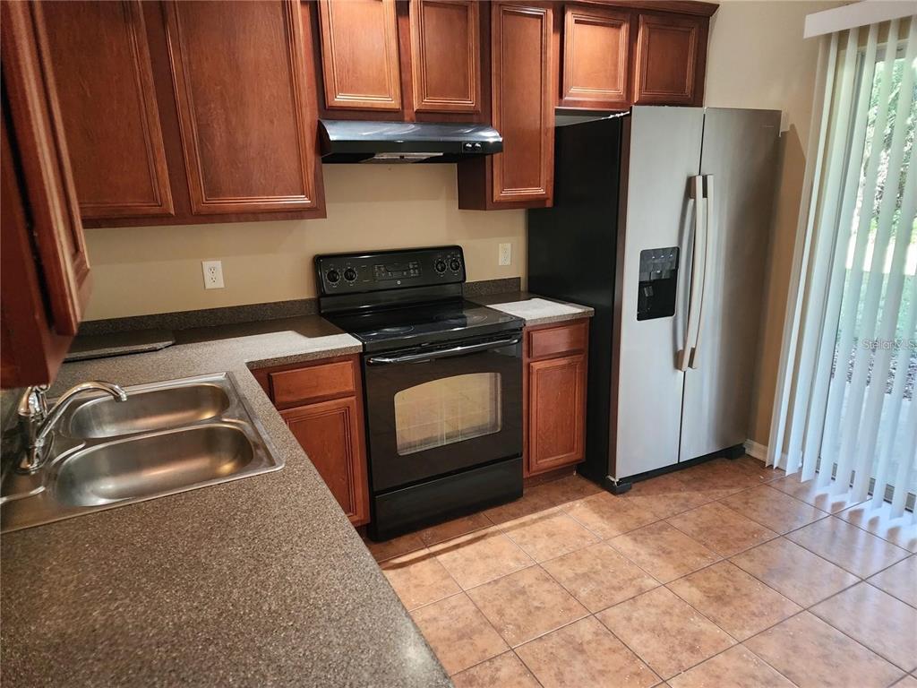 A kitchen features wood cabinets, a black stove, a stainless steel refrigerator, and tiled floors — 15924 FISHHAWK CREEK LANE, LITHIA, FL