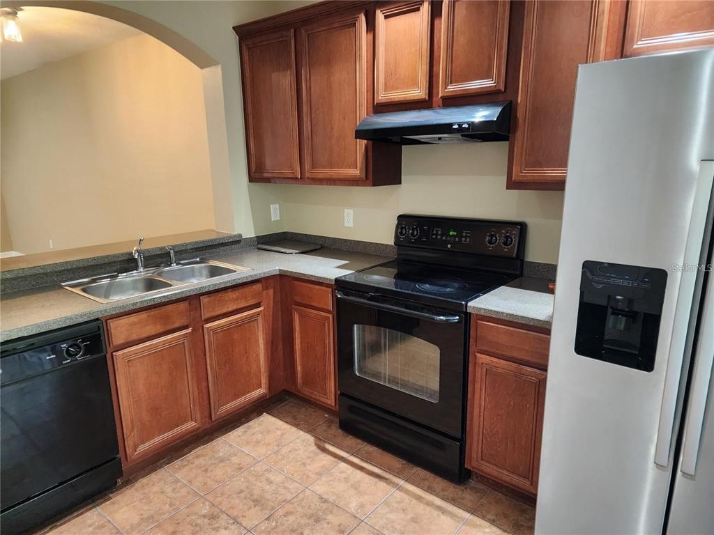 A kitchen features wood cabinets, black appliances, a double sink, and tile flooring — 15924 FISHHAWK CREEK LANE, LITHIA, FL