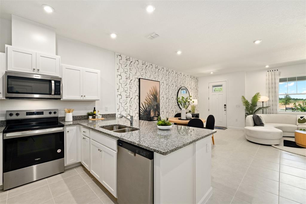 A kitchen with white cabinets and granite countertops opens into a living and dining area — 2796 CAMELLIA FLOWER STREET, APOPKA, FL
