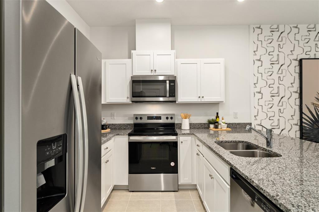 A modern kitchen features white cabinets, granite countertops, stainless steel appliances, and patterned wallpaper — 2796 CAMELLIA FLOWER STREET, APOPKA, FL