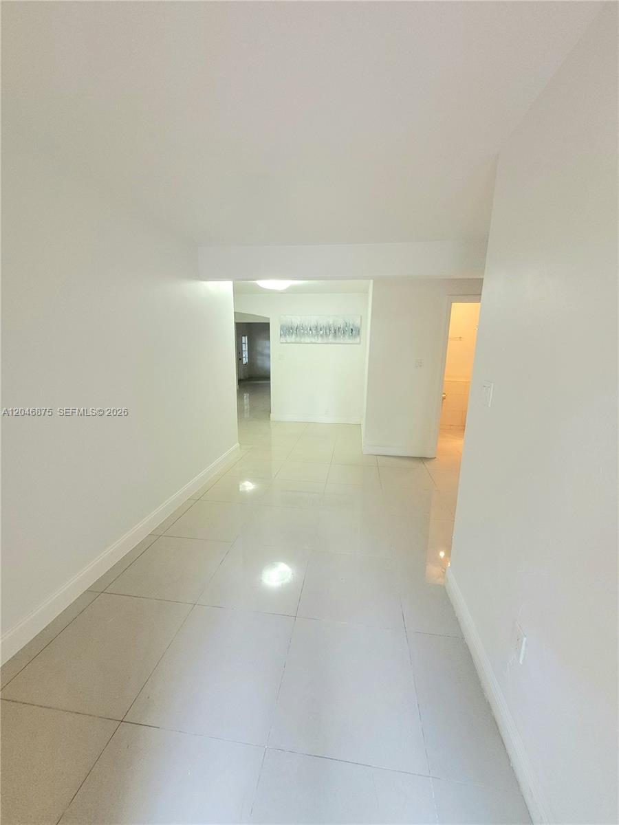 A hallway with white walls and light-colored tile flooring leads toward an open living area — 1132 Moffett St, Hallandale Beach FL 33009, HALLANDALE BEACH, FL