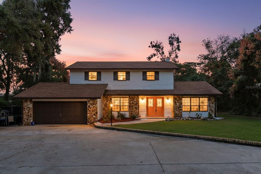 A two-story house with a stone facade, brown roof, and attached garage at sunset — 1416 GROVE AVENUE, LEESBURG, FL