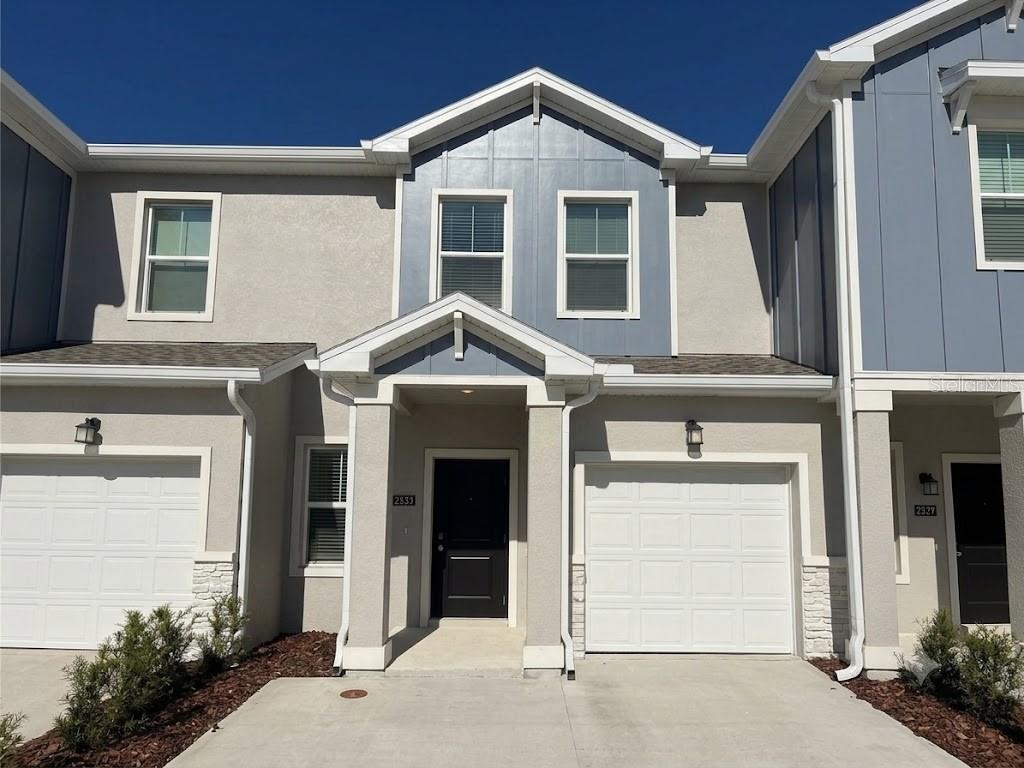 A two-story townhouse exterior features a beige stucco facade, blue siding accents, and two garages — 2533 SKYLINE LOOP, KISSIMMEE, FL