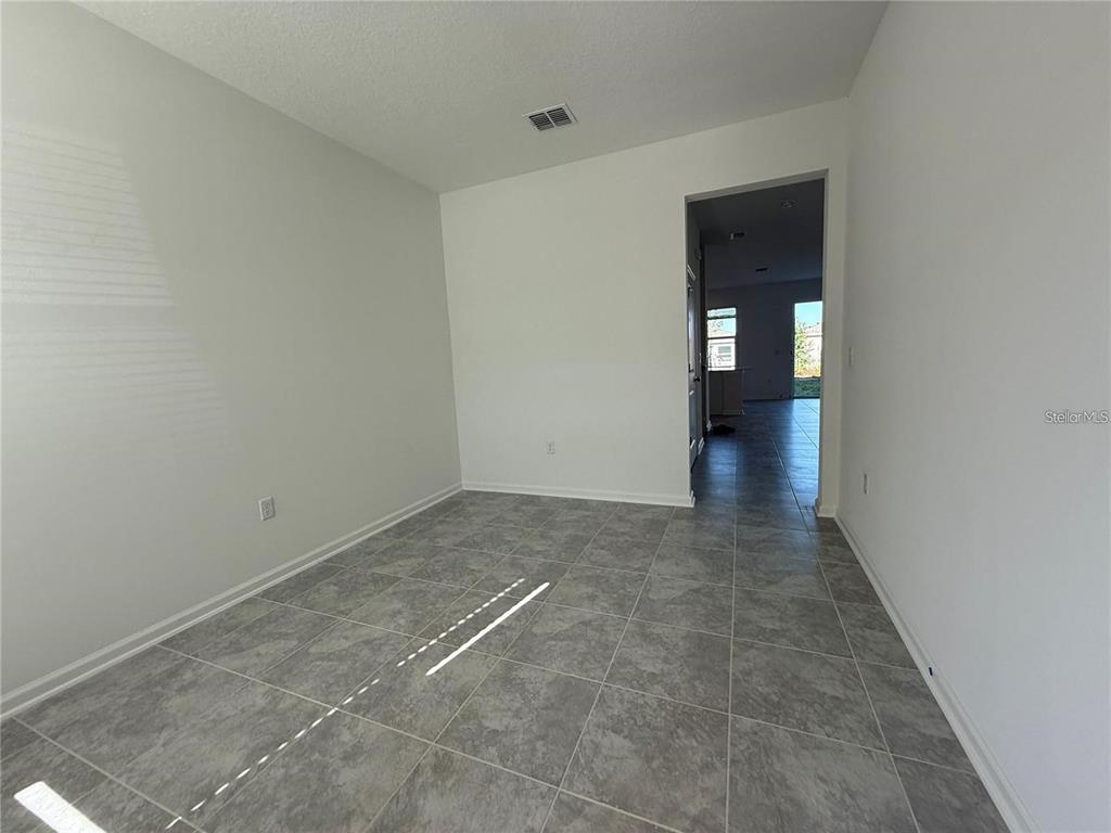 An empty room with gray tile flooring and white walls leads to a hallway — 2533 SKYLINE LOOP, KISSIMMEE, FL