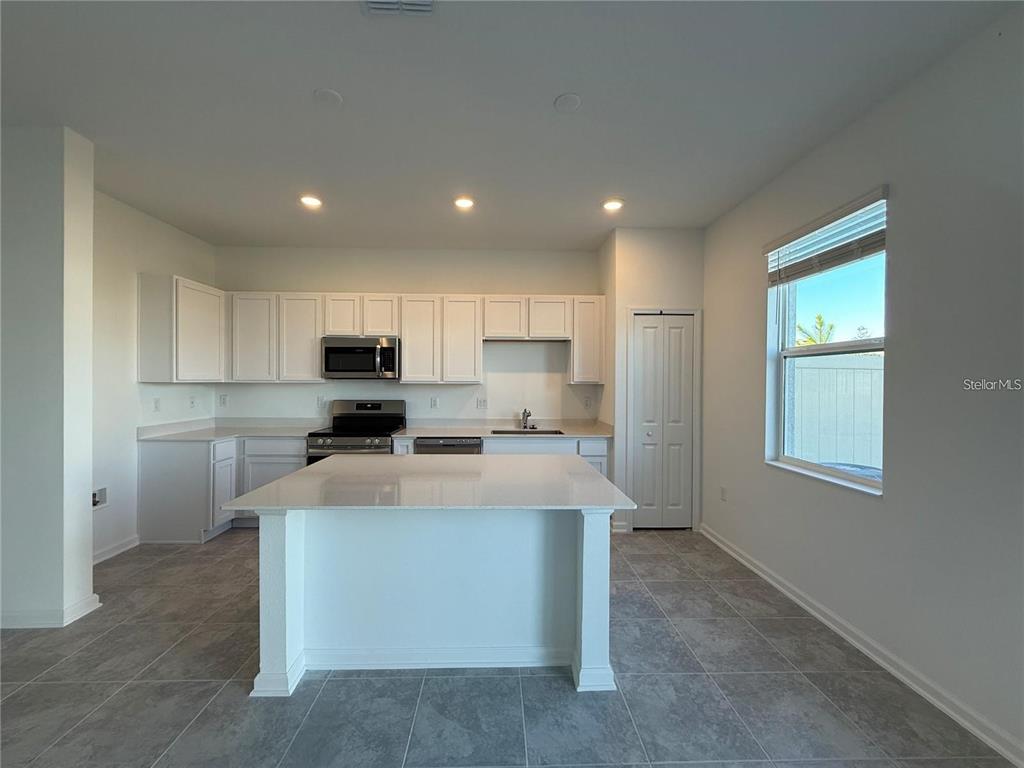 A modern kitchen features white cabinetry, a central island, stainless steel appliances, and tile flooring — 2533 SKYLINE LOOP, KISSIMMEE, FL