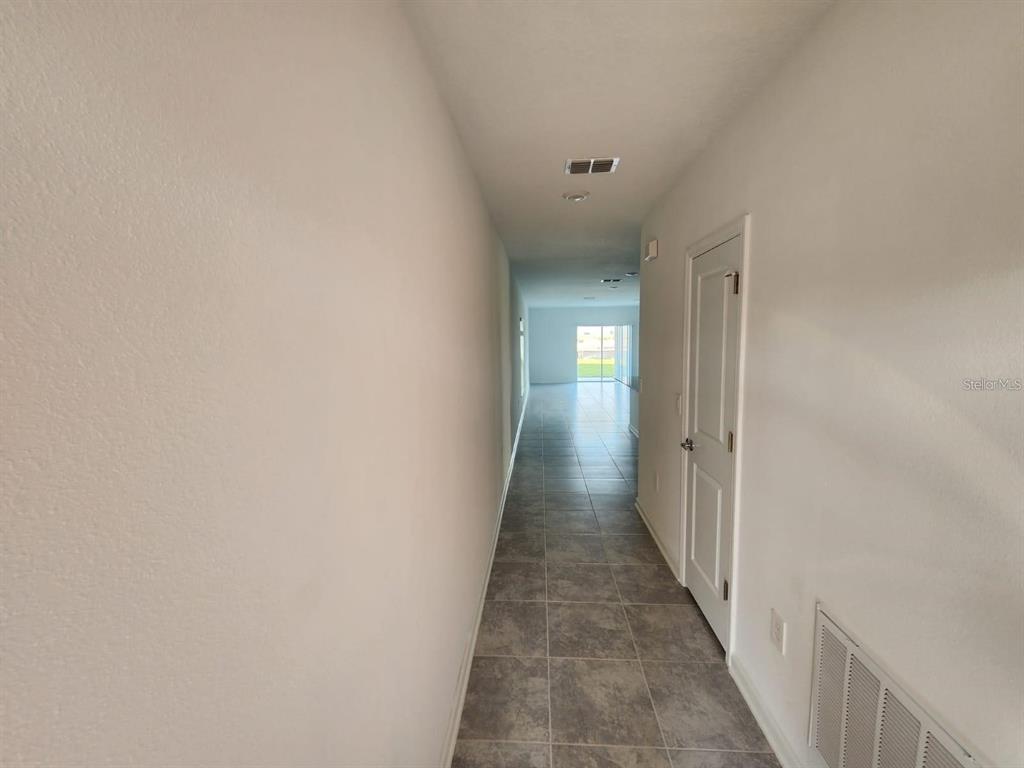 A narrow hallway with gray tile flooring leads toward a bright living area — 2713 RUNNERS CIRCLE, CLERMONT, FL