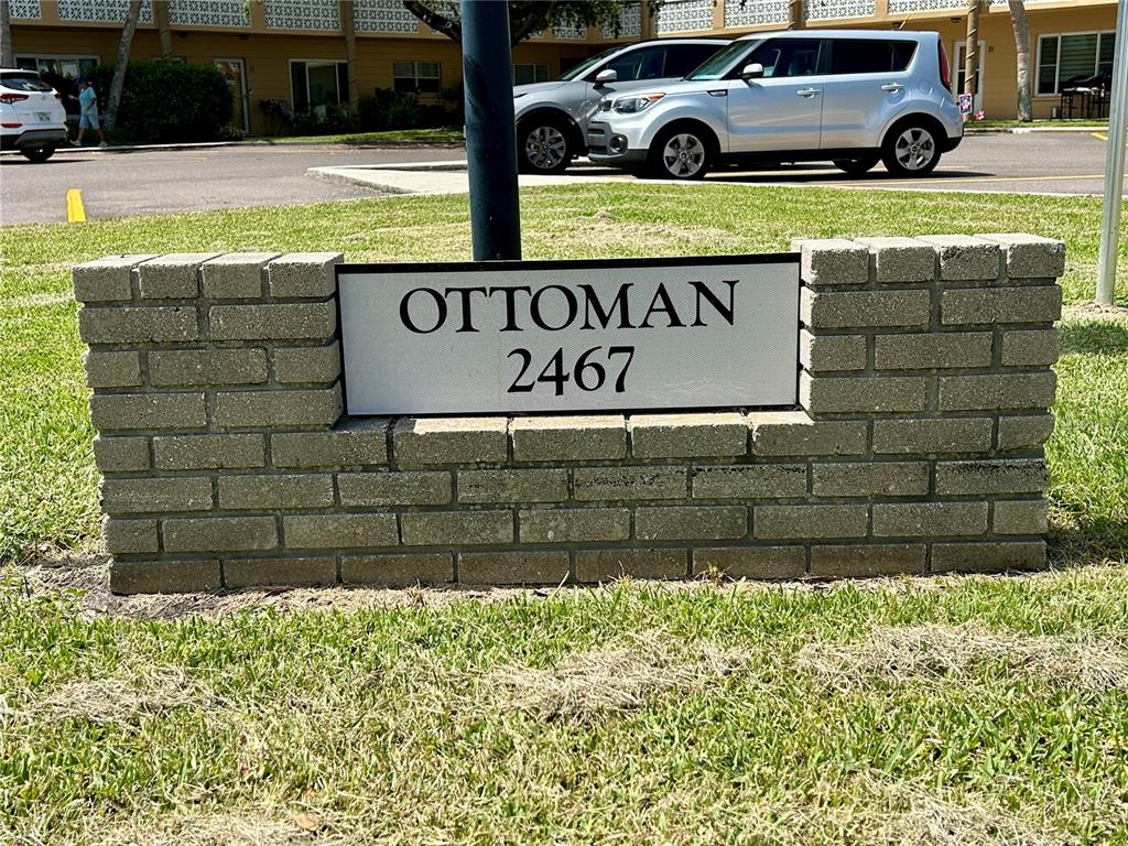 A brick sign displaying the text "OTTOMAN 2467" stands on a grassy lawn — 2467 FINLANDIA LANE UNIT 27, CLEARWATER, FL