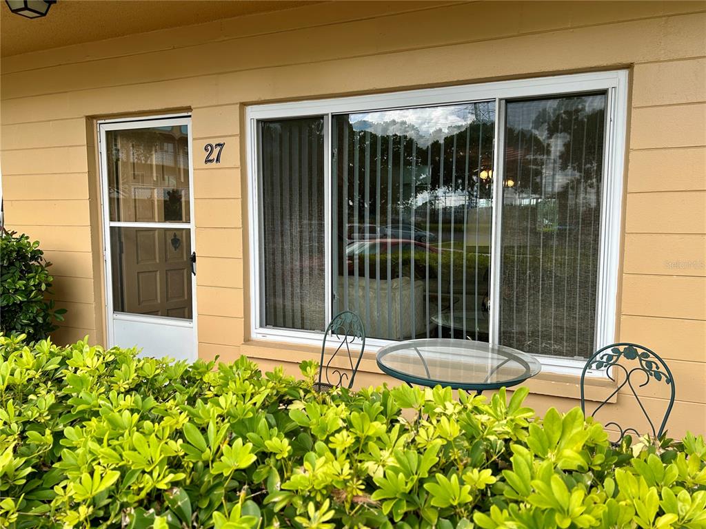 The exterior of a tan building features unit number 27, a glass door, and a window — 2467 FINLANDIA LANE UNIT 27, CLEARWATER, FL