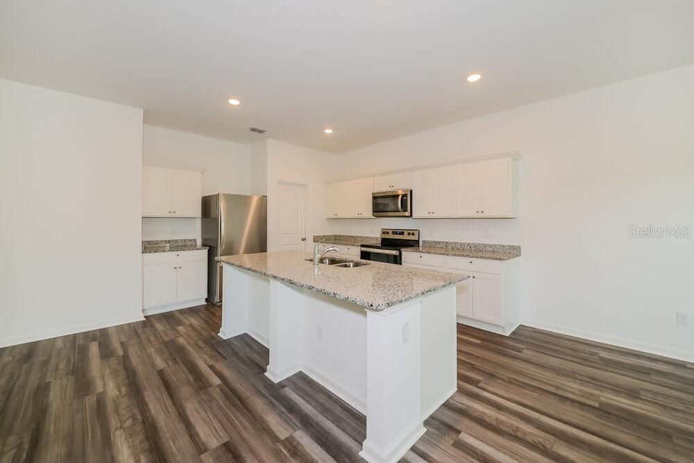 A kitchen features white cabinets, granite countertops, a central island, and wood-look flooring — 996 OCEAN SPRAY DRIVE, RUSKIN, FL